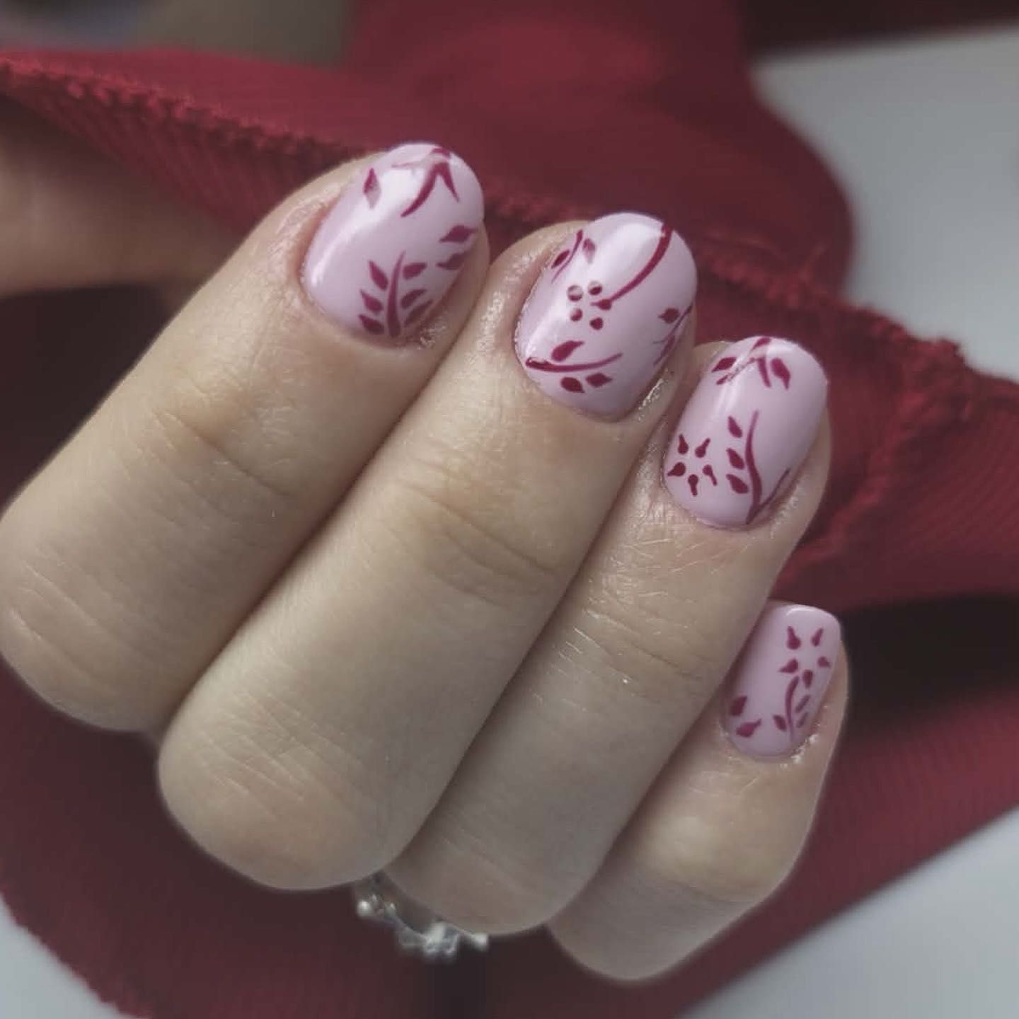 Różowy manicure z bordowym zdobieniem roślinnym